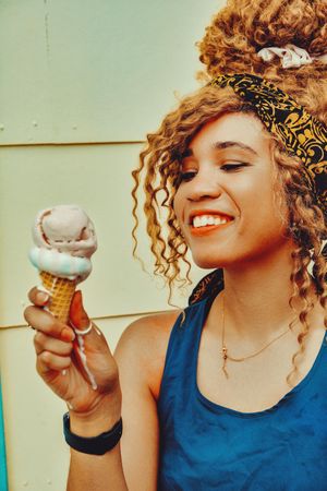 Vertical shot of smiling Black female enjoying an ice cream cone in the sun
