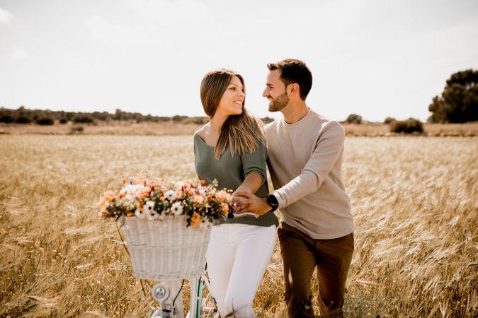 Sincere lovers posing by bicycle on rye field