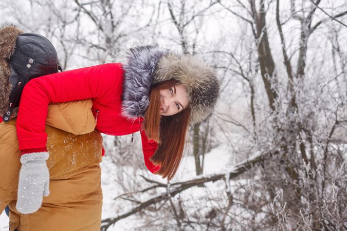 Teenage girl smiling and hanging off other person’s shoulder in snowy forest