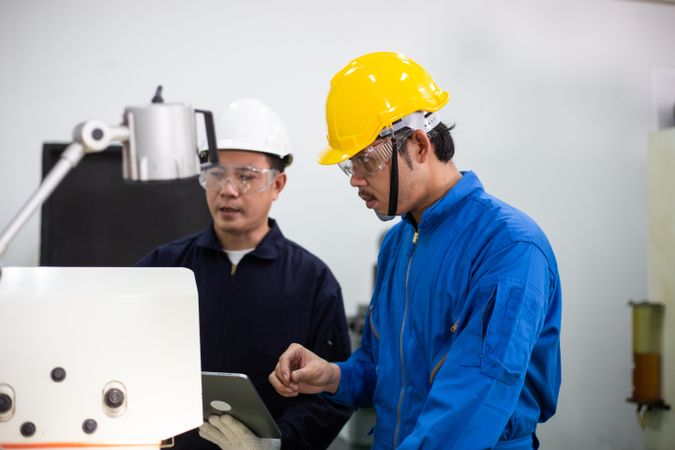 Asian man in blue jumpsuits and hard hats working with machinery