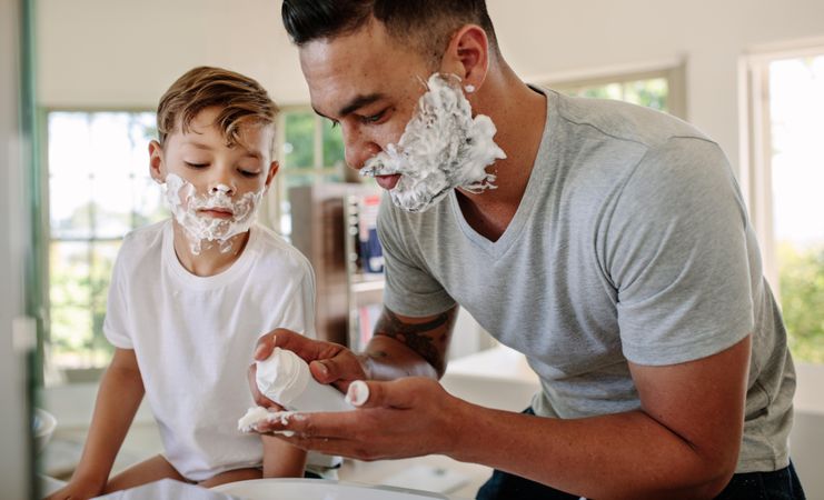 Father and son applying shaving foam on their faces in bathroom