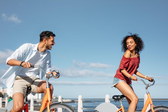 Excited couple riding bicycles in the street with sea in the background