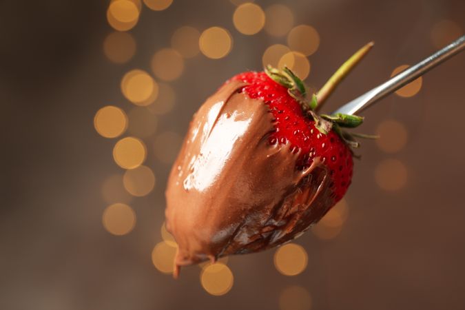 Chocolate fondue. Strawberry in chocolate against brown background with blurred lights