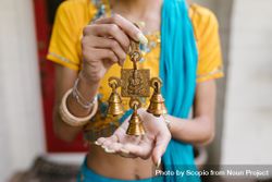 Cropped image of woman in blue and yellow sari holding three bell brass with Ganesha Hindu deity 47q3z0