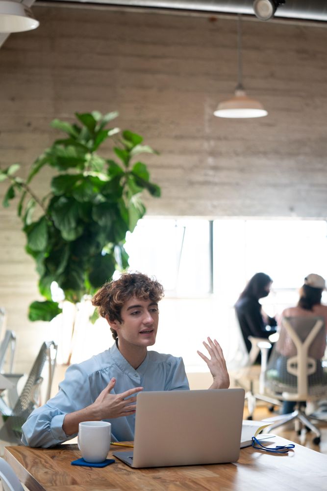 Nonbinary person talking at wooden table in shared workspace