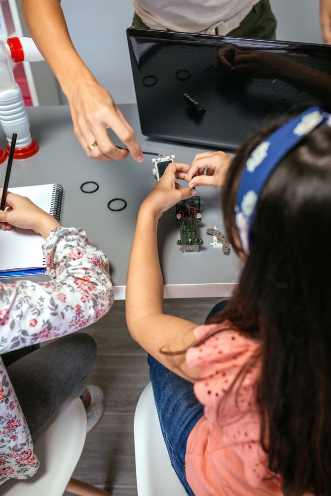 Female teacher helping girl student to assemble electrical circuit in robotics class