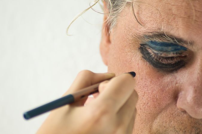 Cropped image of hand applying dark and blue eyeshadow to middle aged man's eyes