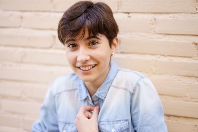 A Cheerful and Young Woman Beaming a Smile While Posing Against a Light Brick Wall