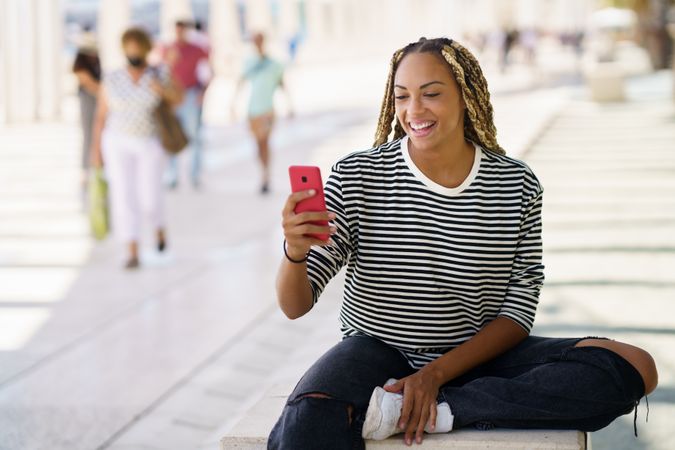 Woman smiling and checking mobile phone while sitting outside