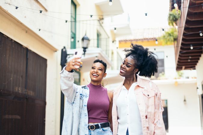 Happy women taking selfies with smartphone walking in the city
