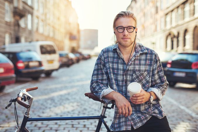 Man in glasses on cobble street leaning on bike