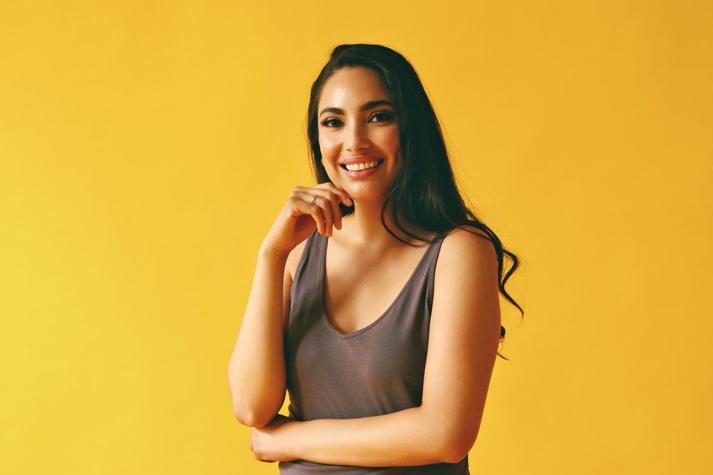 Happy Hispanic woman standing and looking at camera in yellow room, copy space