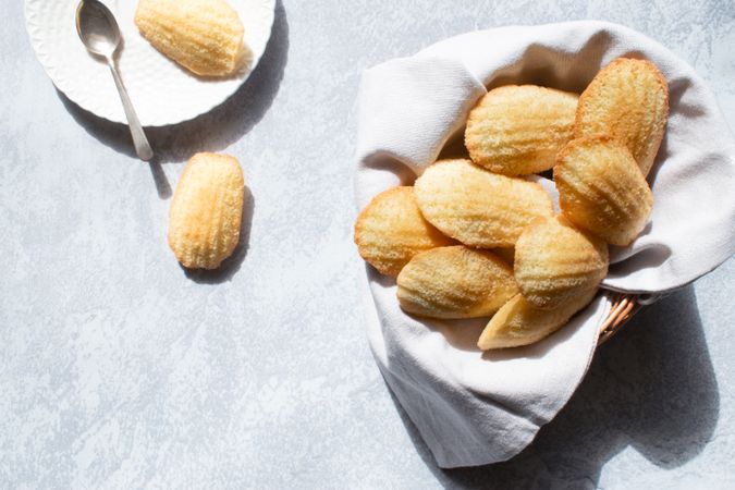 Madeleine cakes in a basket on a grey backdrop.