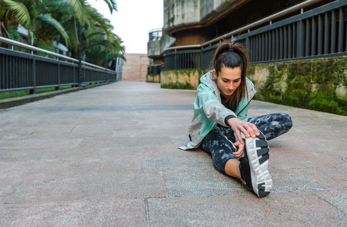 Woman runner looking down while stretching leg before training in town with copy space