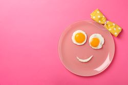 Looking down at pink plate with smiley face on it made of eggs and condiments, copy space
