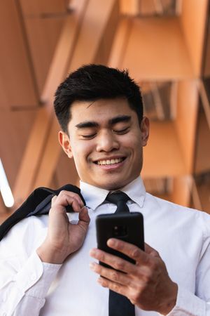 Cheerful Asian male entrepreneur browsing smartphone in city