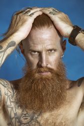 Confident adult red haired hipster touching hair and looking at camera