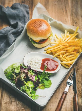Top view of classic hamburger with fries and cottage cheese at wooden restaurant table