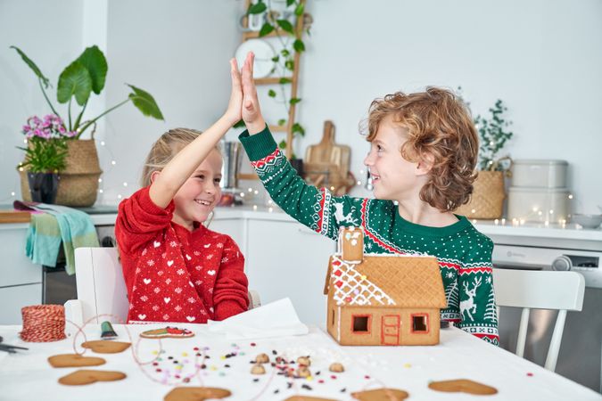 Cheerful siblings giving high five near gingerbread house