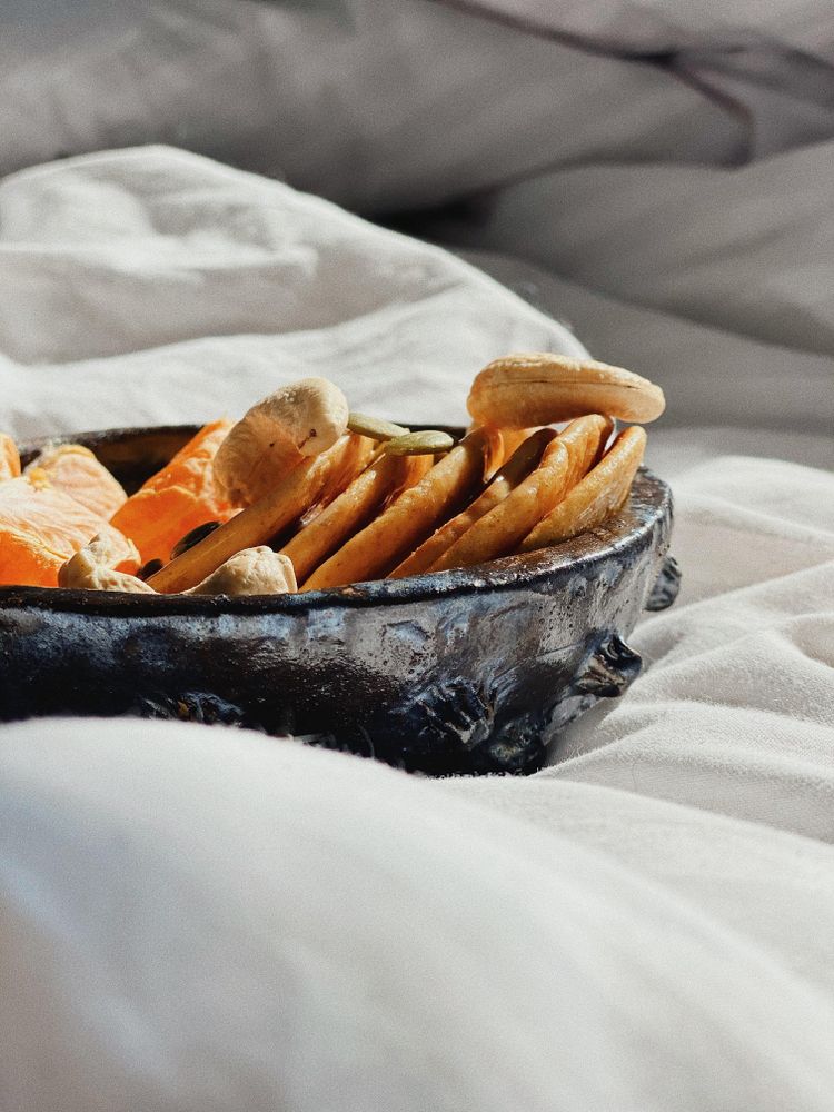 Side view of breakfast bowl of fresh orange slices, nuts and mini pancakes in morning light