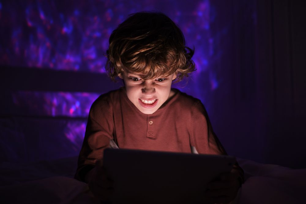 Angry boy browsing tablet in darkness