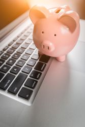 Piggy Bank Resting on Laptop Computer Keyboard.