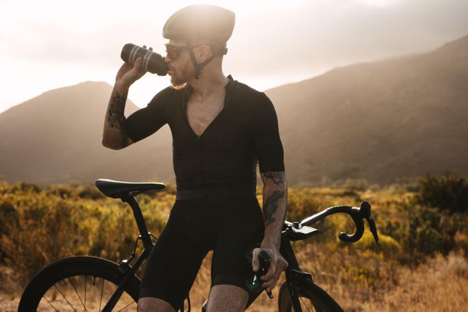 Male athlete taking rest and drinking water outdoors on country road