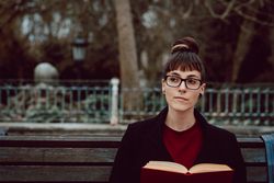 Young woman reading book on bench in park