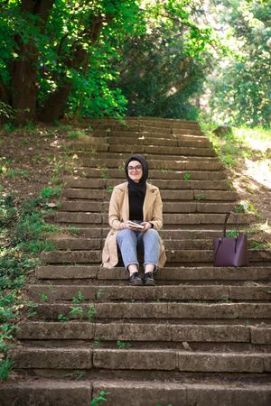 Woman sitting on outdoor stairs looking up from book and smiling