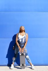 Female in denim overalls standing with skateboard in front of blue building