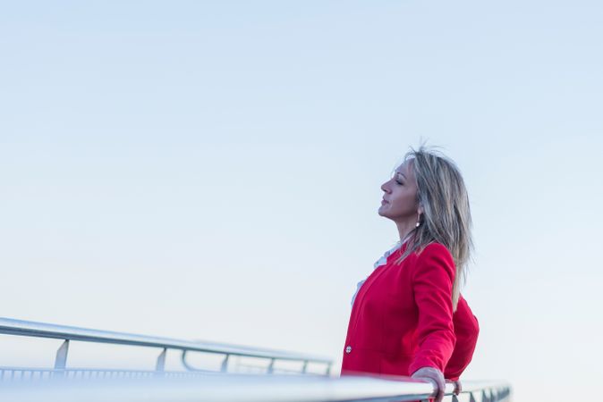 Woman in red coat leaning on railing of pedestrian bridge looking into the distance