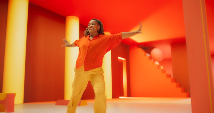 Black Woman in Bright Outfit Dancing Energetically in Geometric Abstract Orange, Yellow Environment. Creative Young Female Performing Modern Dance Choreography in a Spacious Studio