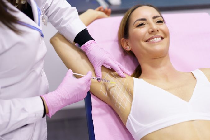 Smiling woman having arm pit injected in clinic