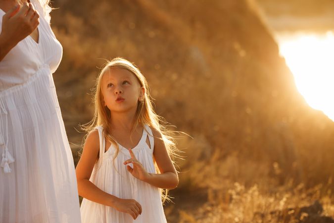 Female child in summer dress looking up at unrecognizable woman outside at dusk