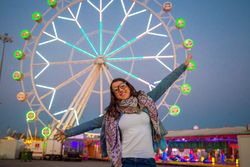 Smiling young woman near illuminated ferris wheel at night