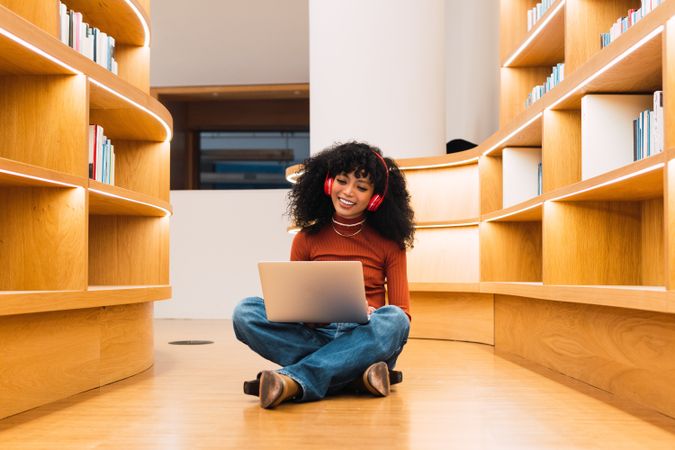 Black woman using laptop in library to music