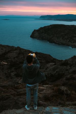 Male taking photo with smartphone overlooking the ocean at dusk