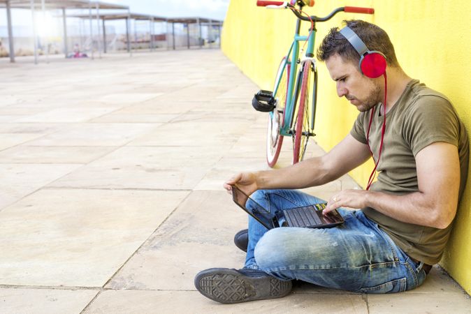 Male with red headphones sitting outside concentrating on laptop