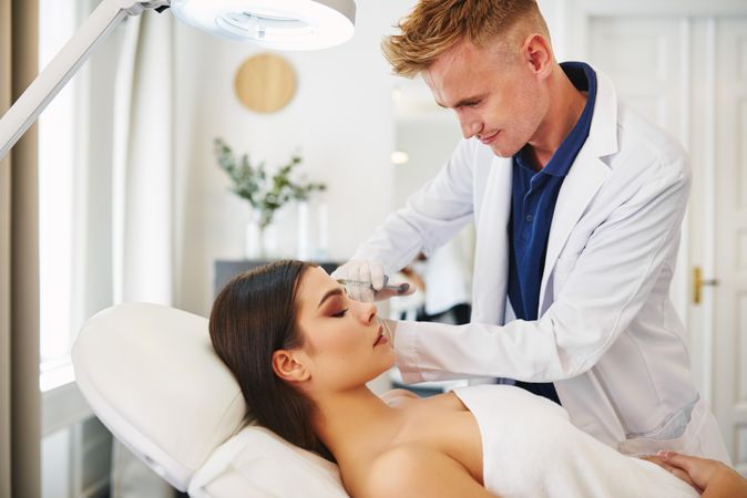 Male dermatologist injecting treatment into brunette patient’s face