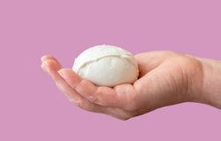 Mozzarella ball in woman hand against a purple background