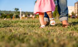 Baby girl learning to walk over a grass park