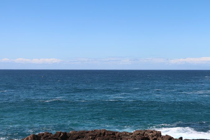 Vast ocean view from rocky shore under a clear blue sky during a sunny day