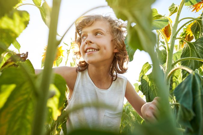 Cheerful child with toothy smile standing near green plants