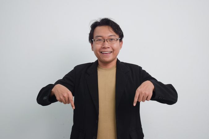 Joyful Asian businessman with suit and casual shirt pointing down