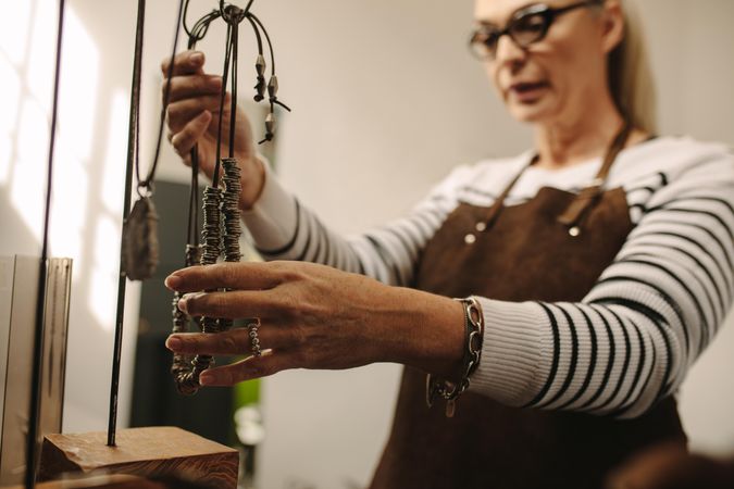 Mature female jeweler hanging a necklace on stand, focus on hands