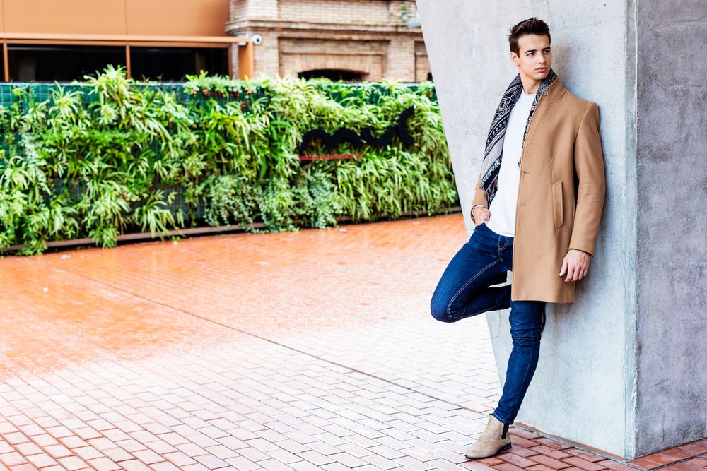 Male wearing winter clothes leaning on wall outside