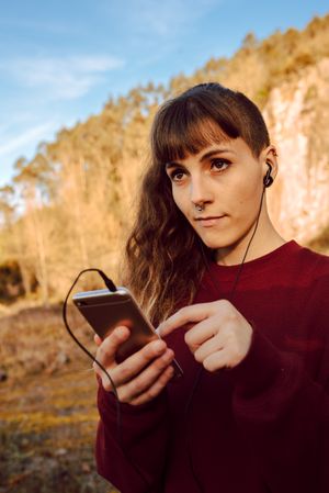 Young woman with piercing listening music on smartphone on hill