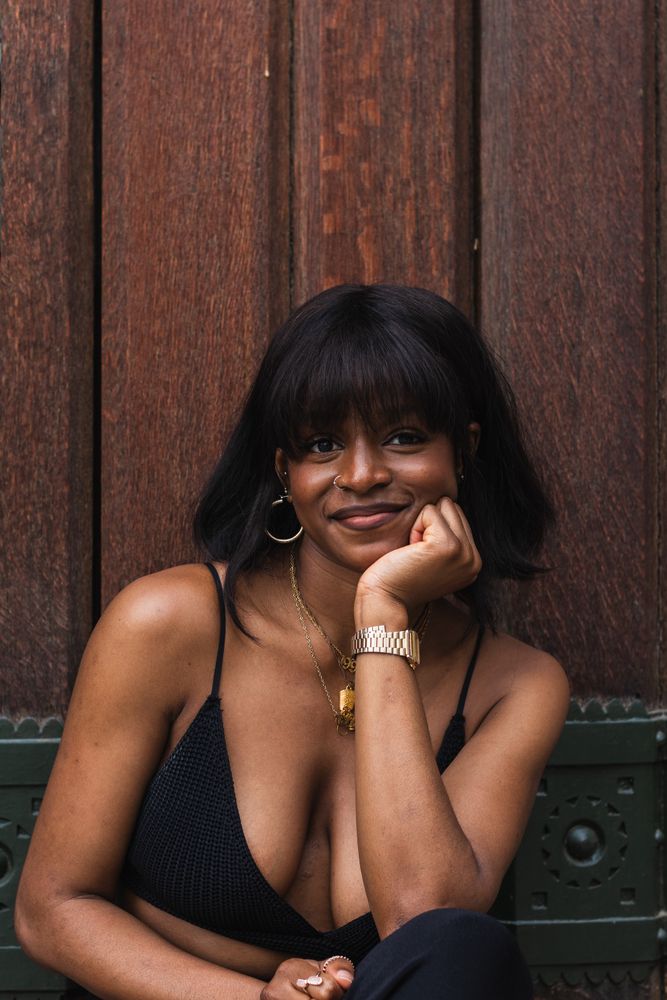 Cheerful Black woman in black outfit against wooden wall