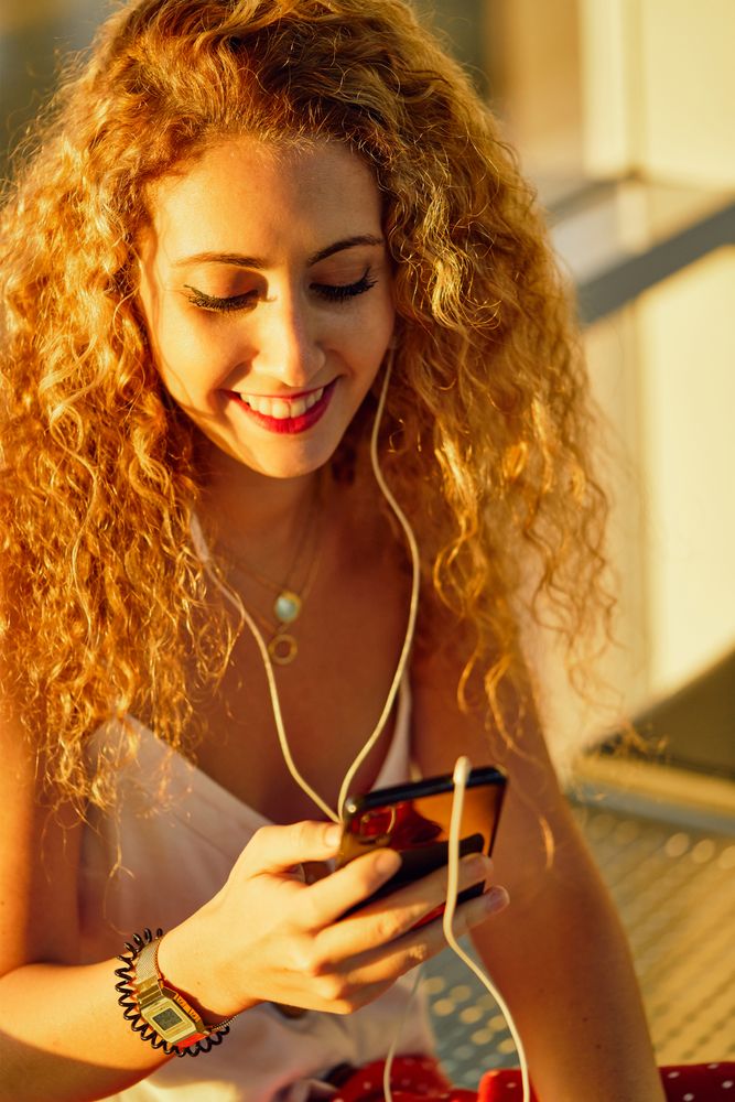 Smiling woman sitting on metal bench with earphones and smartphone