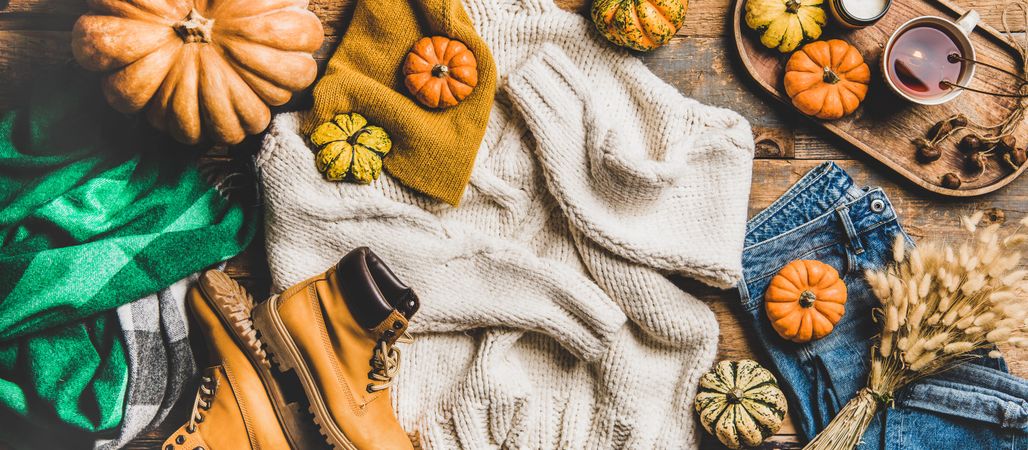 Flat-lay of beige sweater, blue jeans, green scarf, hat, yellow boots, pumpkins and tea